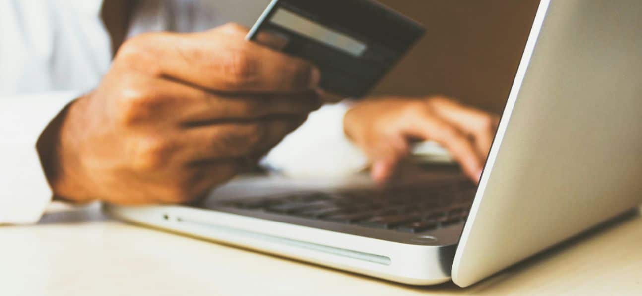 An image including a computer with someone's hand holding a credit card while the other hand is typing on the computer